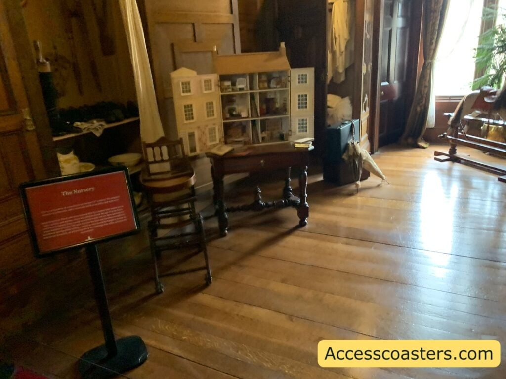  The Royal Weekend Party at Warwick Castle showing a large doll’s house set on a wooden table in an ornate room with polished floorboards, period furniture and an information board explaining the exhibit.