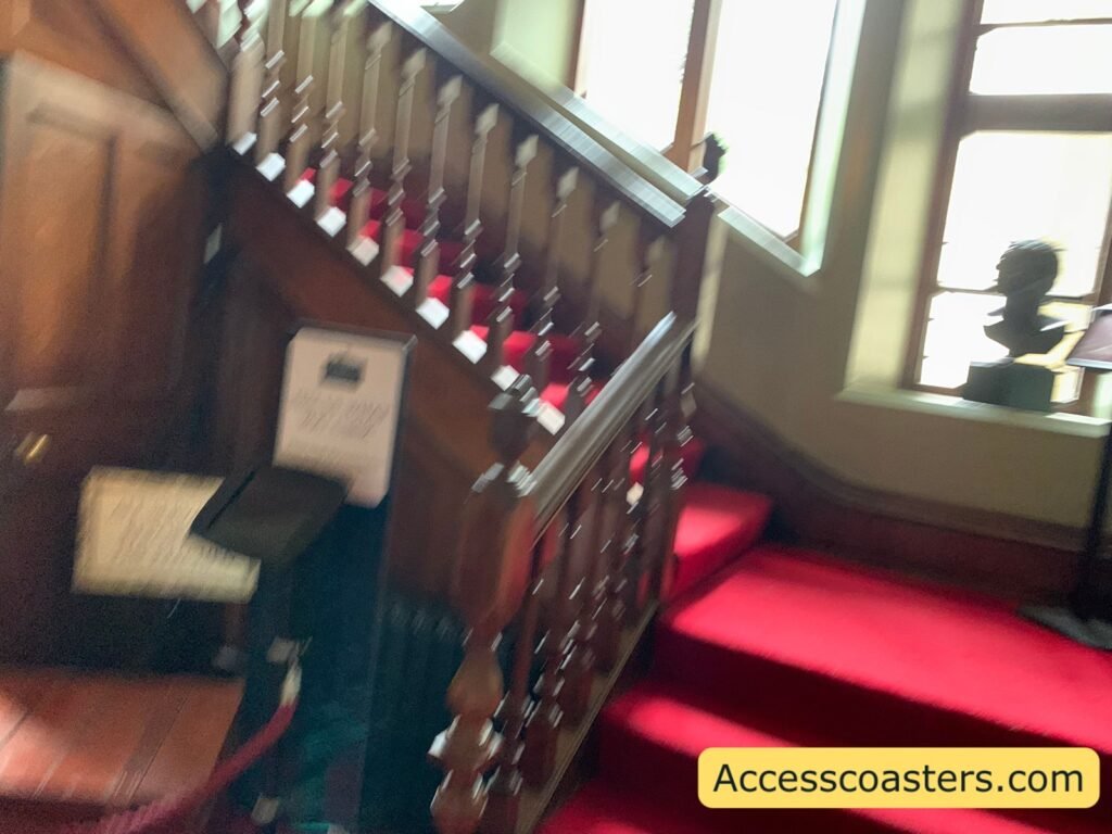 View of the wide wooden staircase leading up to The Royal Weekend Party at Warwick Castle, with red carpet on the steps, a sturdy banister on one side,
