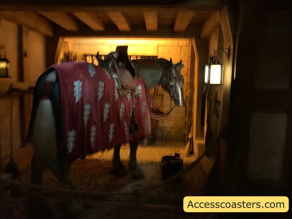 Stable display in The Kingmaker featuring a life-sized model horse covered in a rich red heraldic caparison