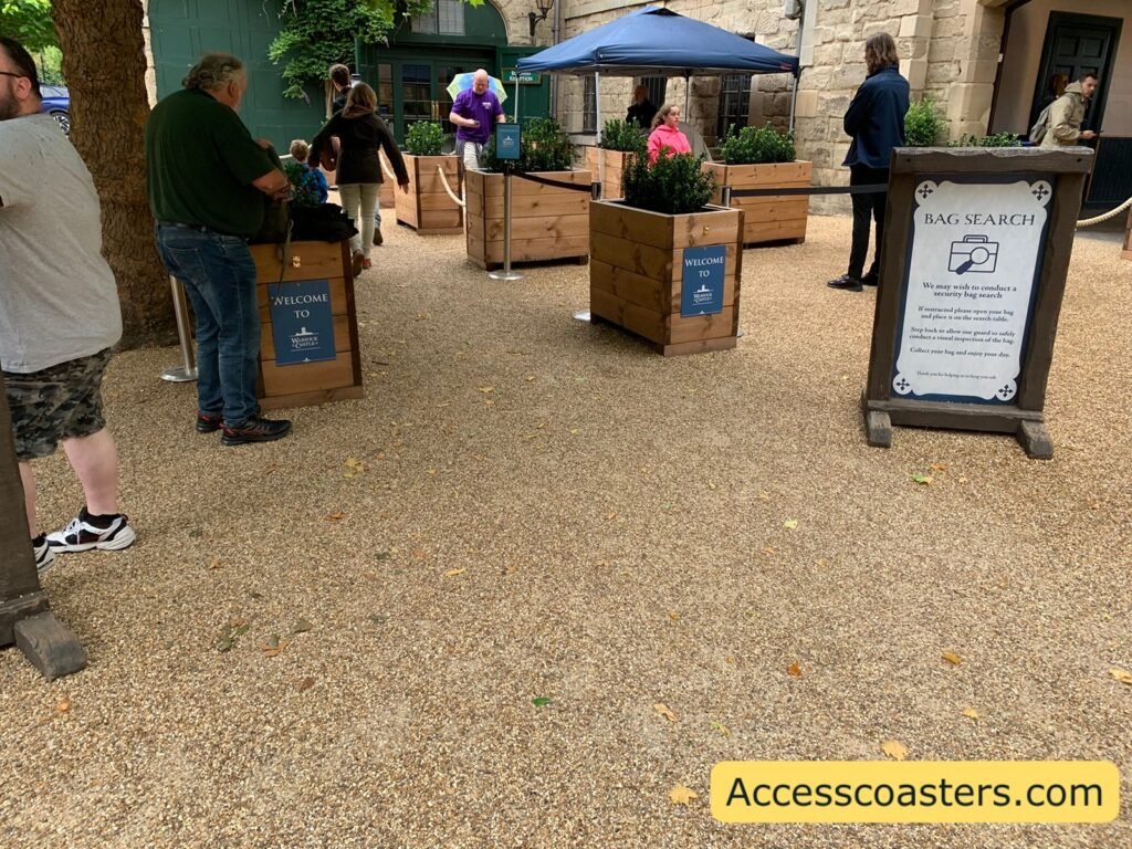 entrance to bag check area with a queue line rapped out and a sign explain bag checks.  a blue gazebo can be see with a table underneath and a security guard. 