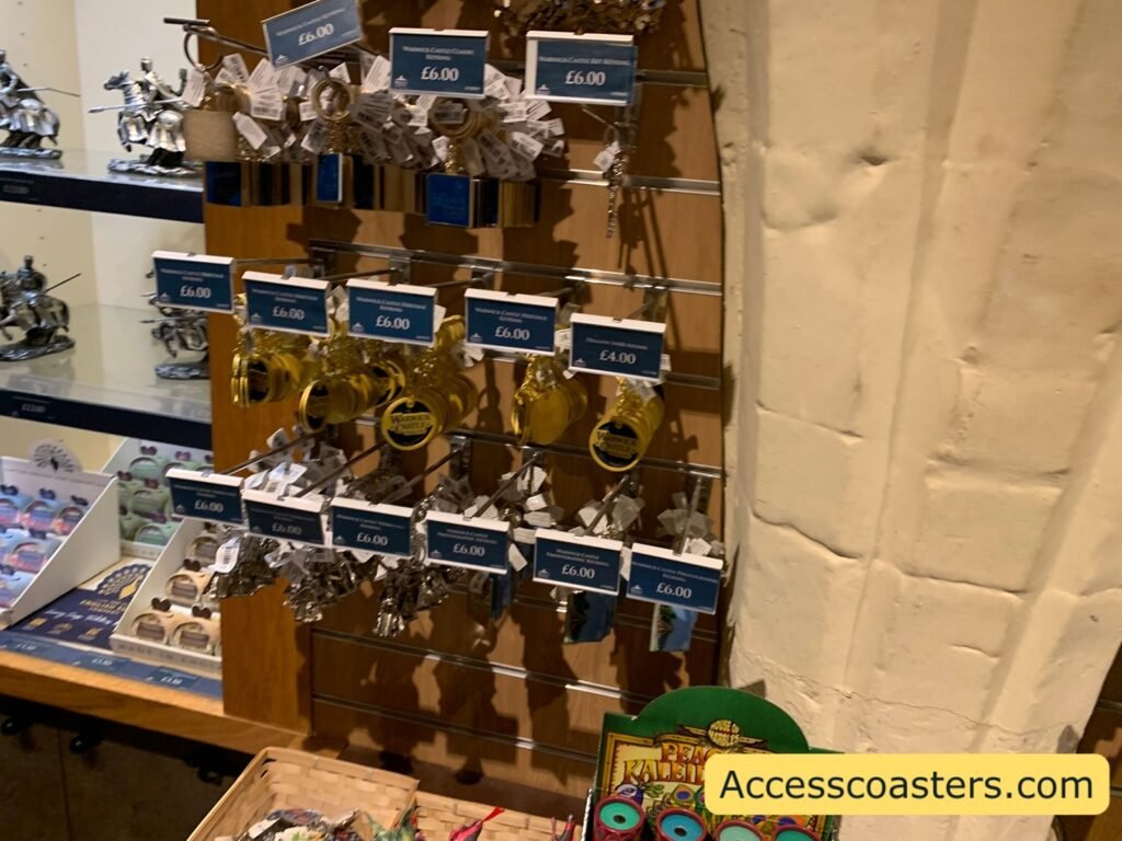 Gift shop display of Warwick Castle souvenirs including metal keyrings and small figures hanging on hooks with blue price tags.
