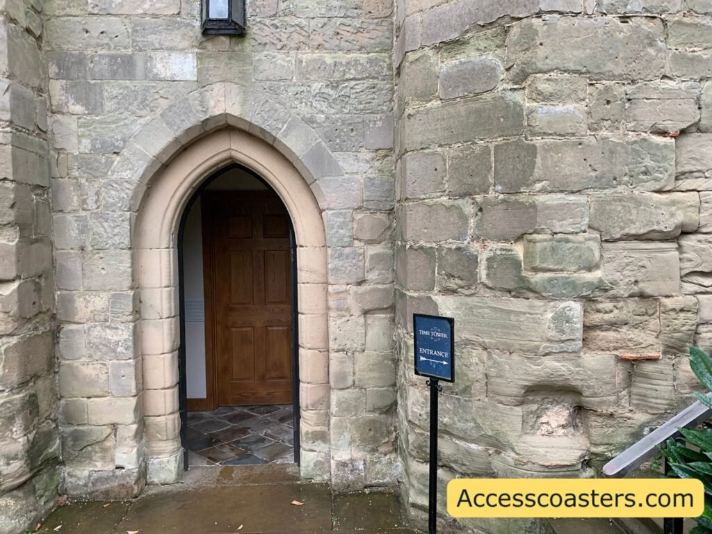 Stone archway entrance in the base of Warwick Castle’s Time Tower, with a wooden door and small sign outside, showing where the Welfare and Sensory Room is located 