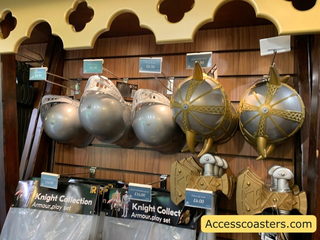 Row of silver and gold toy knight helmets and round shields with Warwick Castle branding