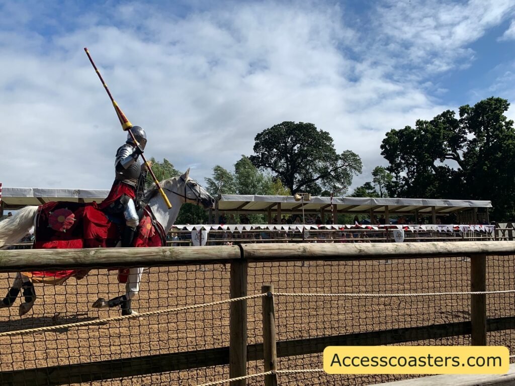 Armoured knight on a horse draped in red, raising a long jousting lance in the Wars of the Roses Live arena