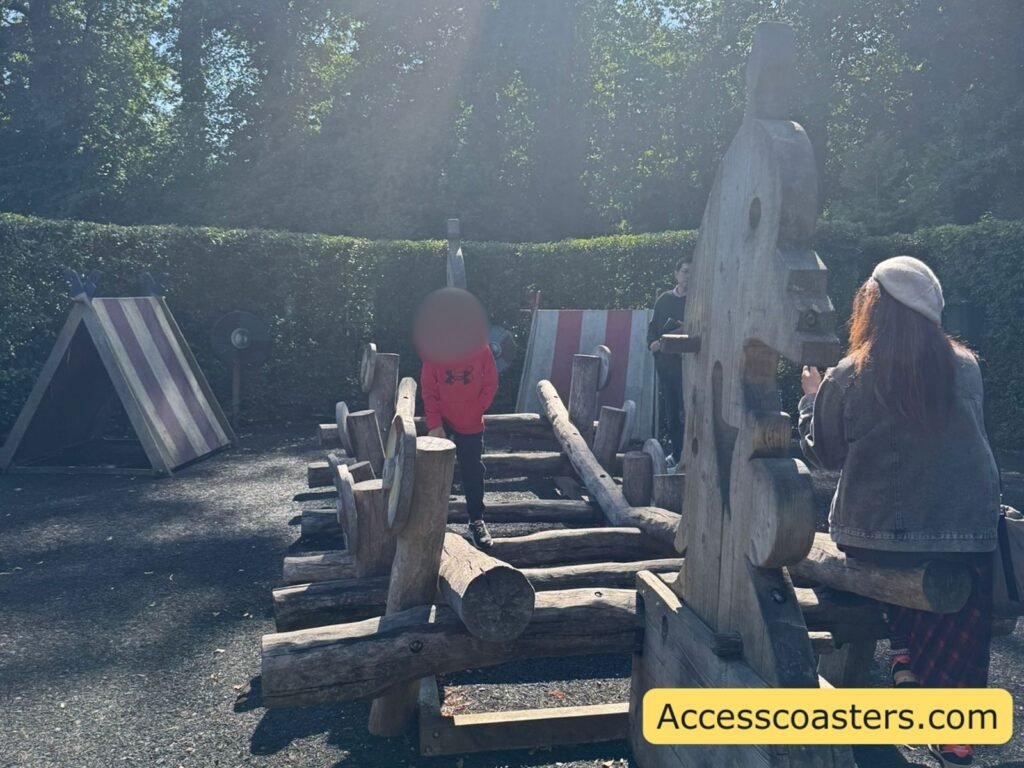 a Viking style play area on  gravel with several chunky wooden structures in a row and some little red and white huts, 