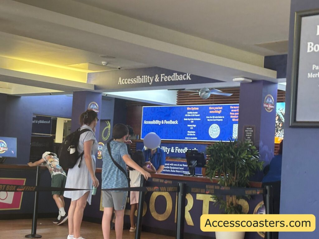 counter inside the box office with digital screen explain the access options a text that reads accessibility and feedback. there is a queue of people being served at the box office. 
